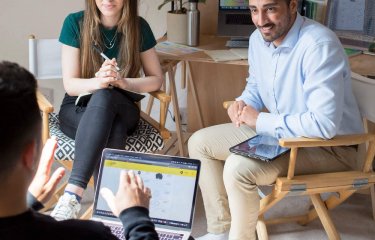 Three people seated in conversation with graphs and a plant in the background